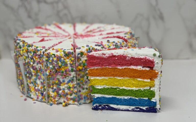 Cinotti's Kayla Cake: Wholesale 6 rainbow colored layers of vanilla cake iced in white buttercream then garnished with rainbow sprinkles. Sliced 14